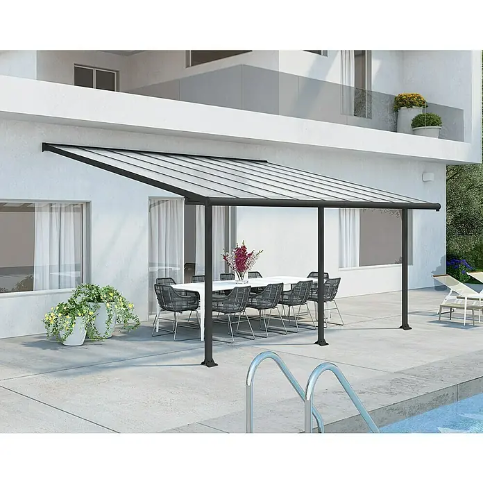 Palram – Canopia Terrassenüberdachung Olympia - B x T: 546 x 300 cm, Anthrazitgrau, Polycarbonat, Transparent - Bild einer modernen Terrassenüberdachung mit klarem Dach und schwarzen Rahmen, die einen stilvollen Essbereich im Freien beschattet.