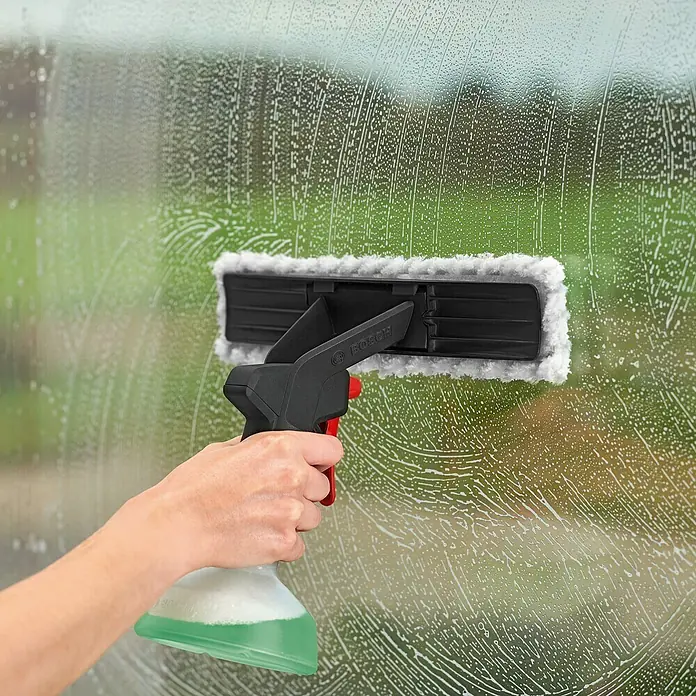 Bosch Akku-Fenstersauger GlassVac Set - 3,6 V, 2 Ah - Bosch Window Spray mit Reinigungspad in Aktion auf einer Glasoberfläche, die mit Reiniger bedeckt ist.