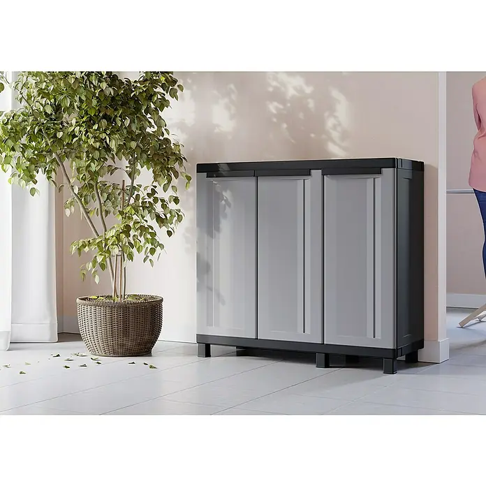 Terry Kunststoff-Mehrzweckschrank Twist Black 102B - L x B x H: 39 x 102 x 91,5 cm - Schrank mit drei grauen Türen und schwarzem Rahmen neben einem geflochtenen Pflanzgefäß mit einem grünen Baum.