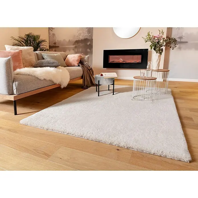 Voltomat HEATING Stand- & Wandkamin Flat - Schwarz, 26 x 128 x 61 cm - Ein flauschiger, hellgrauer Teppich liegt auf einem Holzboden und verleiht dem Wohnraum eine gemütliche Atmosphäre.