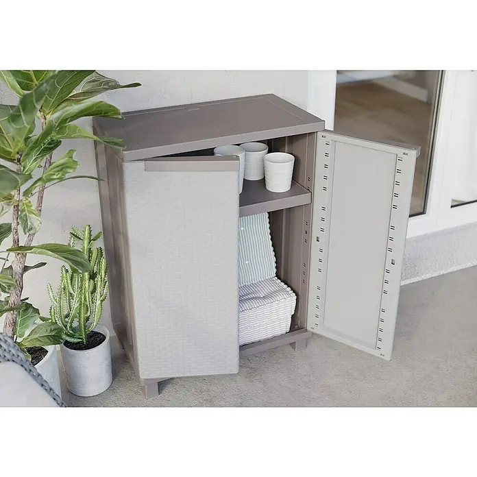 Terry Ratán Kunststoff-Mehrzweckschrank J Rattan 68 - L x B x H: 37,5 x 68 x 91,5 cm - Der graue Kunststoffschrank mit offenen Regalen und einer Tür steht auf einem grauen Untergrund. Pflanzen sind daneben platziert.