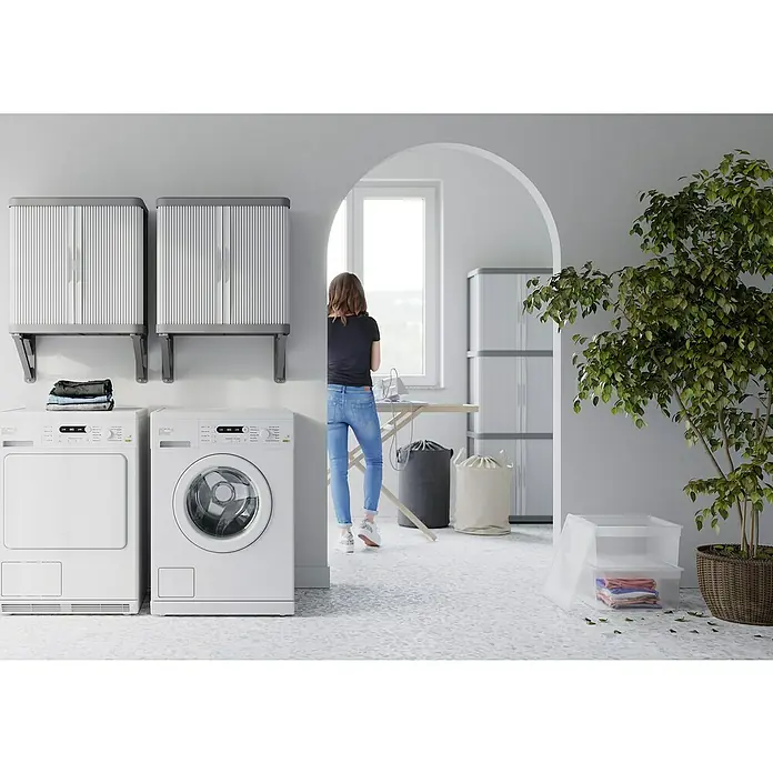 Terry Armario multiusos de plástico  Rolling Space - L x An x Al: 36 x 59 x 59,5 cm - Lavadero con lavadora, secadora y armarios de almacenamiento. La habitación también tiene una persona planchando ropa.