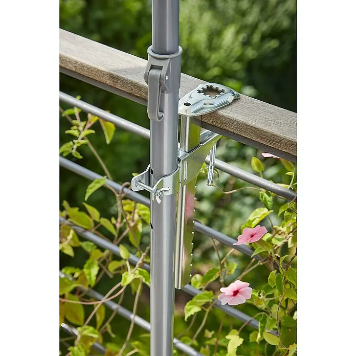 Sunfun Balkonklammer - Grau, Für Rohrdurchmesser: 25 mm - 32 mm - Nahaufnahme einer grauen Schirmhalterung, die an einem Holzzaun befestigt ist, mit Blumen und Grün im Hintergrund.