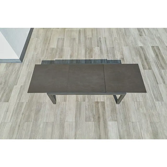 Sunfun Maja Gartentisch Stone - L x B x H: 300 x 100 x 74 cm, Aluminium, Sintered Stone, Ausziehbar, Night-Grey - Ein dunkler, erweiterbarer Esstisch mit Metallgestell steht auf einem hellen Holzboden. Der Tisch ist schlicht und modern gestaltet.