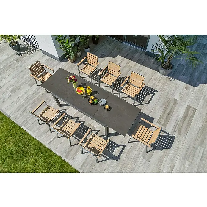 Sunfun Gartenmöbel-Set Maja Stone/Carina - 9 -tlg., Sintered Stone/Aluminium/Akazie/Stahl, Tischplatte ausziehbar, Anthrazit/Teak - Ein einladender Außenbereich mit einem Esstisch-Set, umgeben von Pflanzen. Der graue Tisch mit Holzstühlen lädt zum Verweilen ein.