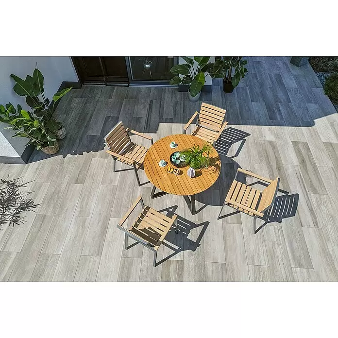 Sunfun Carina Gartentisch rund - Ø x H: 115 x 76 cm, Akazienholz, Teak - Hölzerne Terrassen-Essgruppe mit rundem Tisch und fünf Stühlen auf gefliester Terrasse, umgeben von Topfpflanzen.