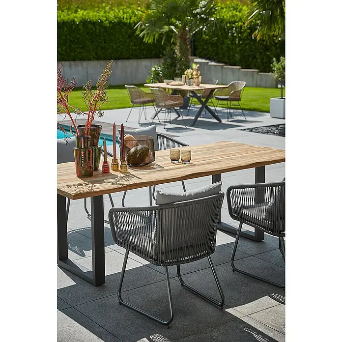 Sunfun Maja Gartenmöbel-Set - 6 -tlg., Baumkante/U-Gestell, Teak/Edelstahl/Kunststofffaser-Schnüre, Teak/Grau - Ein moderner Gartentisch mit Stühlen, dekoriert mit Vasen und Kerzen, steht auf einer Terrasse, ideal für Mahlzeiten im Freien.