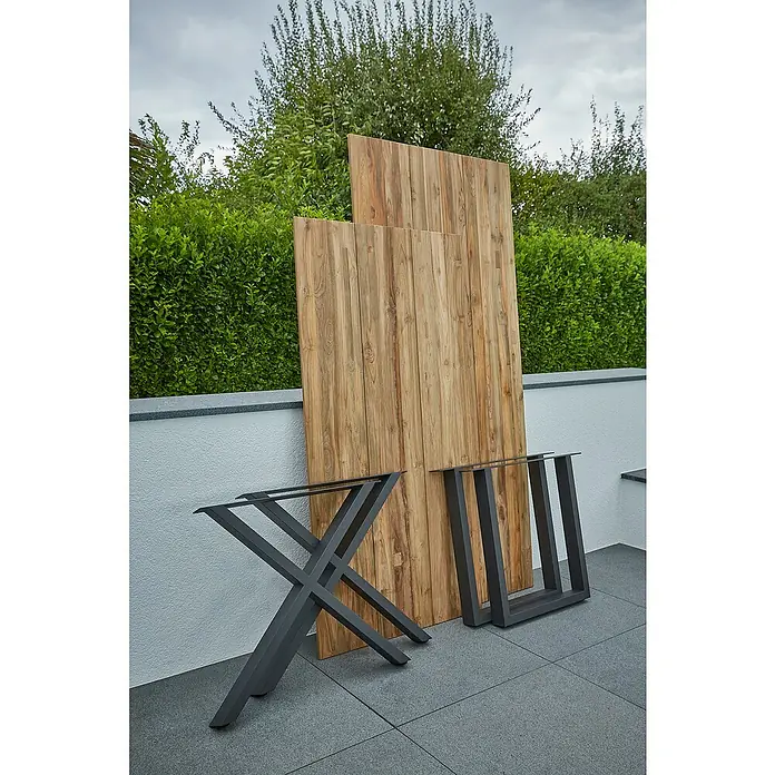 Sunfun Garten-Tischplatte220 x 100 cm, Teakholz, Baumkante - Tischplatten aus Holz und Tischbeine aus Metall stehen auf einer Terrasse bereit für den Zusammenbau eines Gartentisches.