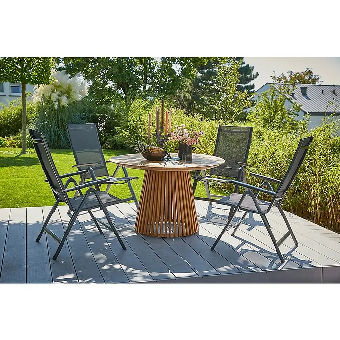 Sunfun Gartenmöbel-Set Osby/Maja - 5 -tlg., Teak/Aluminium/Textilen, Teak/Anthrazit - Eine runde Gartentischgruppe aus Holz mit vier grauen Stühlen auf einer Terrasse im Freien, umgeben von üppigem Grün.