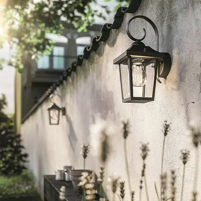 Philips Außenwandleuchte - 60 W, 14,3 x 17,8 x 30,8 cm, IP44 - Schwarze, klassische Wand-Außenleuchte mit Klarglas, beleuchtet eine Gartenmauer.