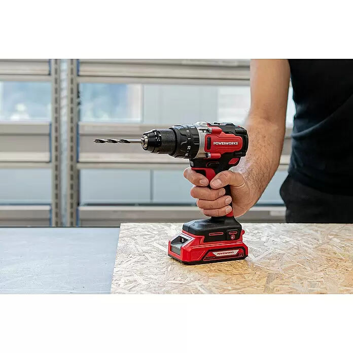Powerworks -  - Eine Person hält eine rot-schwarze Powerworks Akku-Bohrmaschine mit Bohrer über einer Holzplatte.