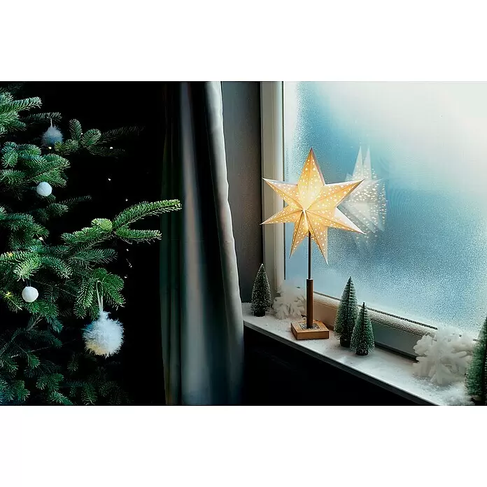Markslöjd Standstern Solvalla - Weiß, Netzbetrieben - Eine beleuchtete Papiersterndekoration mit Holzfuß auf einer verschneiten Fensterbank, neben einem Weihnachtsbaum.