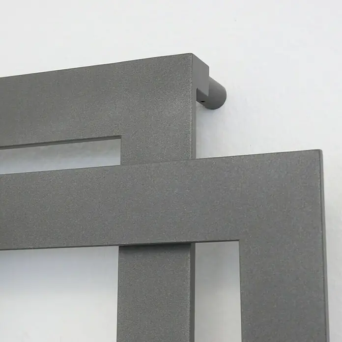 Szagato Designheizkörper Art II - B x H: 600 x 1.800 mm, Wärmeleistung bei Vorlauftemperatur von 75 °C (D: 50): 1.019 W, Moonstone-Grau - Nahaufnahme eines modernen, grauen Heizkörpers mit rechteckigen Ausschnitten, der an einer weißen Wand montiert ist.