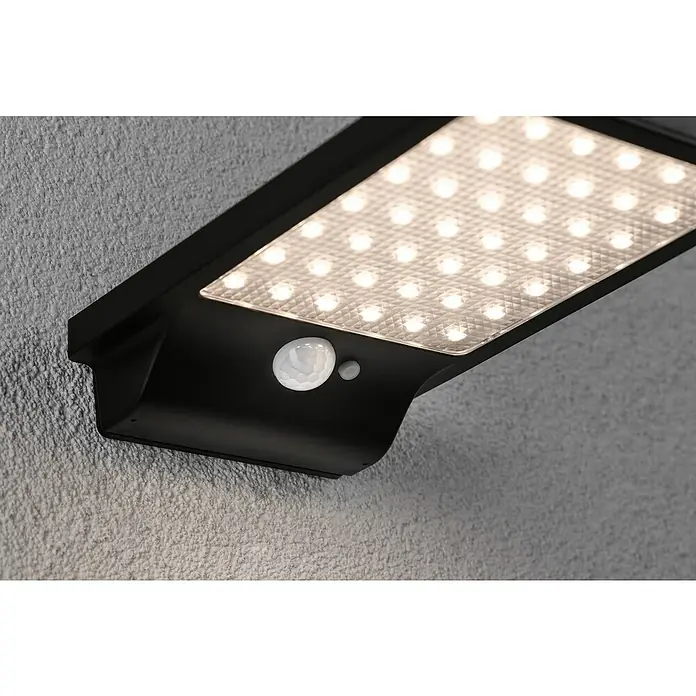 Paulmann Solar-Außenwandleuchte Solveig - Max. Systemleistung: 4,8 W, L x B x H: 17,3 x 10,5 x 2,9 cm, Schwarz, Lichtstrom: 338 lm - Nahaufnahme einer schwarzen Solar-Wandleuchte mit Bewegungsmelder und hellem LED-Panel an einer strukturierten Wand.