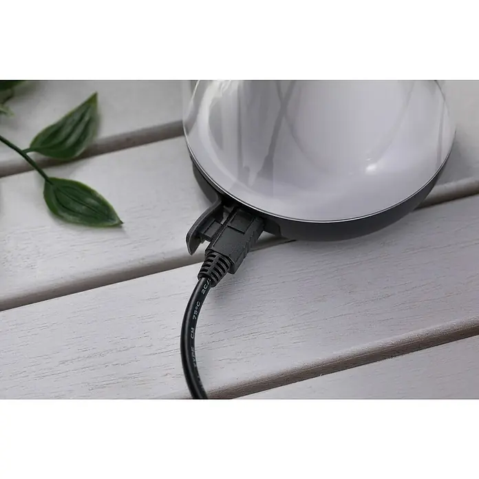 Paulmann Akku-Tischleuchte Cupulino - 1,3 W, Anthrazit, Warmweiß, 8,3 x 18,4 cm - Nahaufnahme einer weißen Aroma-Diffuser-Basis mit einem schwarzen Netzkabel, das an eine USB-Buchse angeschlossen ist, auf einem Holztisch.