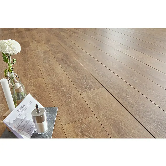 LOGOCLIC Ambienta Laminatmuster Eiche Corno - 296 x 195 x 1 mm, Landhausdiele - Einladendes Bild mit Laminatboden, der eine warme Atmosphäre schafft. Dekorative Elemente wie Blumen und Kerze setzen Akzente.