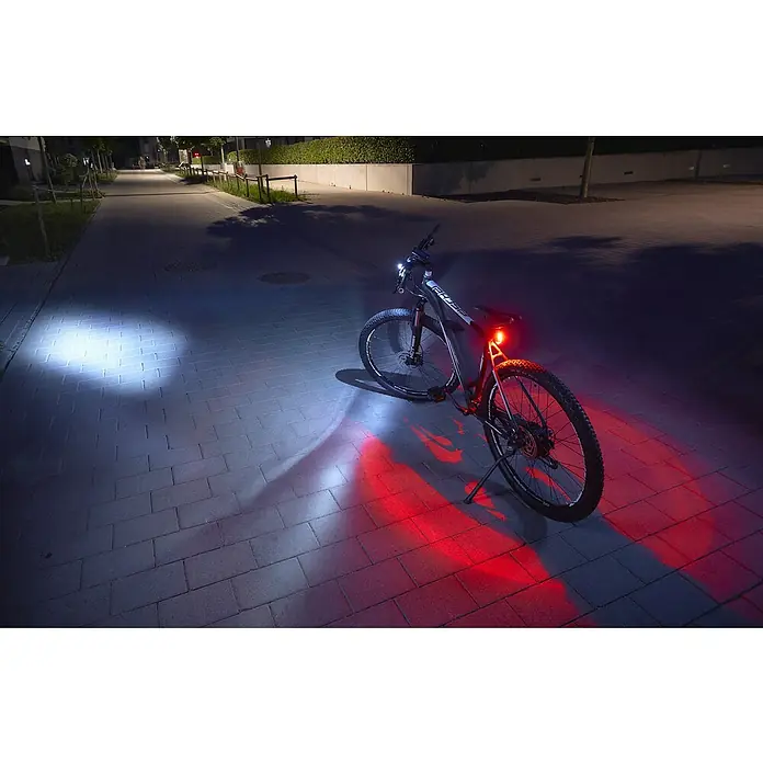 Fischer Fahrradbeleuchtungs-Set - 60 lx, LED, Schwarz - Ein schwarzes Fahrrad mit eingeschalteten Vorder- und Rückleuchten, die den Weg beleuchten, für sicheres Fahren bei Dunkelheit.