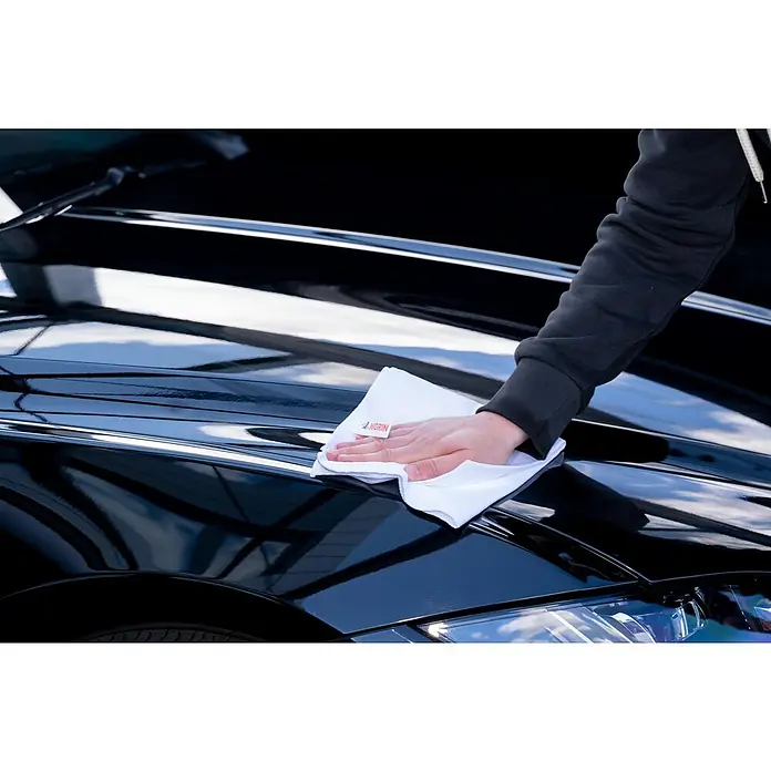 Nigrin Performance Versiegelung Ceramic - 750 ml - Nahaufnahme einer Person, die ein schwarzes Auto mit einem weißen Nigrin-Mikrofasertuch abwischt, um es zu reinigen und zu polieren.