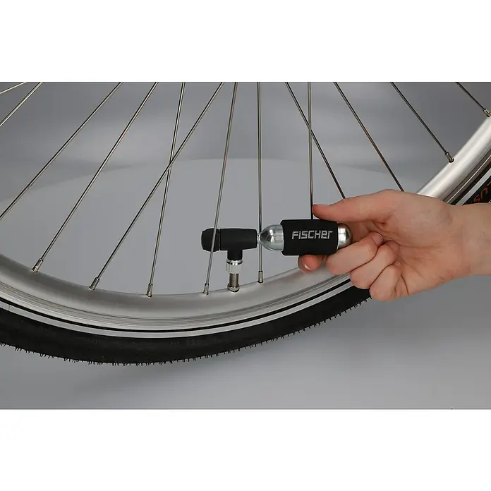 Fischer Mini-Luftpumpe CO2 - Geeignet für: Dunlopventile - Eine Hand hält einen Fischer CO2-Inflator, der an einem Fahrradreifen befestigt ist, um den Reifen aufzupumpen.