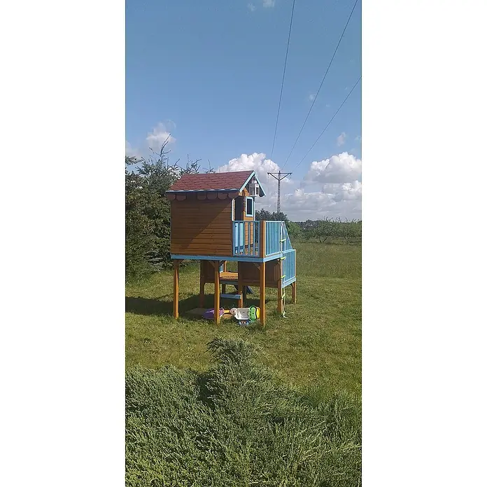 Spielhaus Tom 60 - L x B x H: 226,5 x 176 x 272 cm, Holz, Natur/Rot - Ein charmantes hölzernes Spielhaus mit blauen Akzenten und einer kleinen Leiter in einer grünen Gartenumgebung.