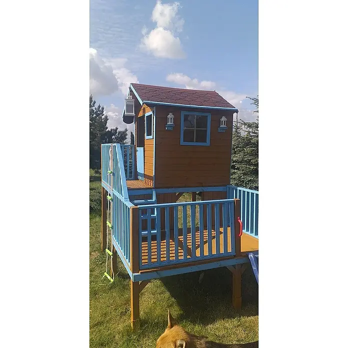 Spielhaus Tom - L x B x H: 226,5 x 176 x 272 cm, Holz, Natur - Holzspielhaus mit blauen Akzenten und einer Rutsche im Garten. Das Spielhaus hat ein braunes Dach und kleine Laternen.