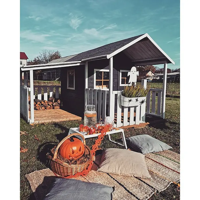 Erweiterungsmodul für Spielhaus Leonie - 150 x 106 x 120 cm, Holz, Natur, Passend für: Spielhaus Leonie - Halloween-Dekoration vor einem Spielhaus. Ein Korb mit Kürbis und Kissen liegen auf einer Decke mit Halloween-Girlande, um eine festliche Atmosphäre zu schaffen.