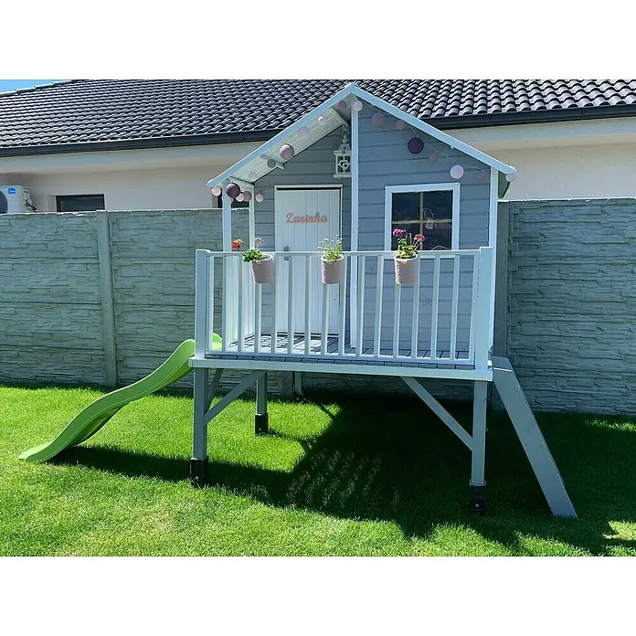 Kinderspielturm Jeremy - L x B x H: 175 x 226 x 250,5 cm, Natur - Dieses Bild zeigt ein charmantes Spielhaus für Kinder mit einer Rutsche und einem kleinen Balkon, geschmückt mit Blumen und Lichtern.