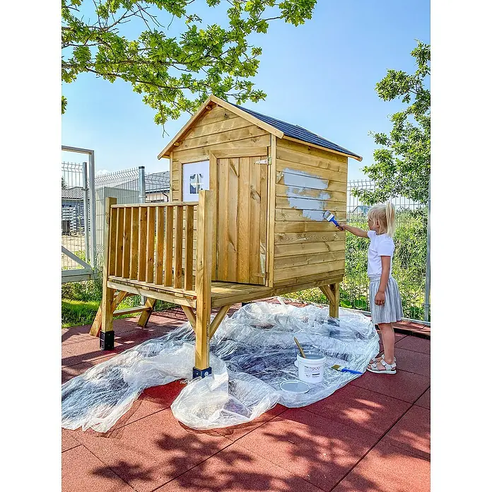 Spielhaus Tobias - L x B x H: 179 x 161 x 221 cm, Holz, Natur - Ein Kind streicht ein Holzspielhaus mit grauer Farbe. Im Vordergrund liegt eine Plastikplane.