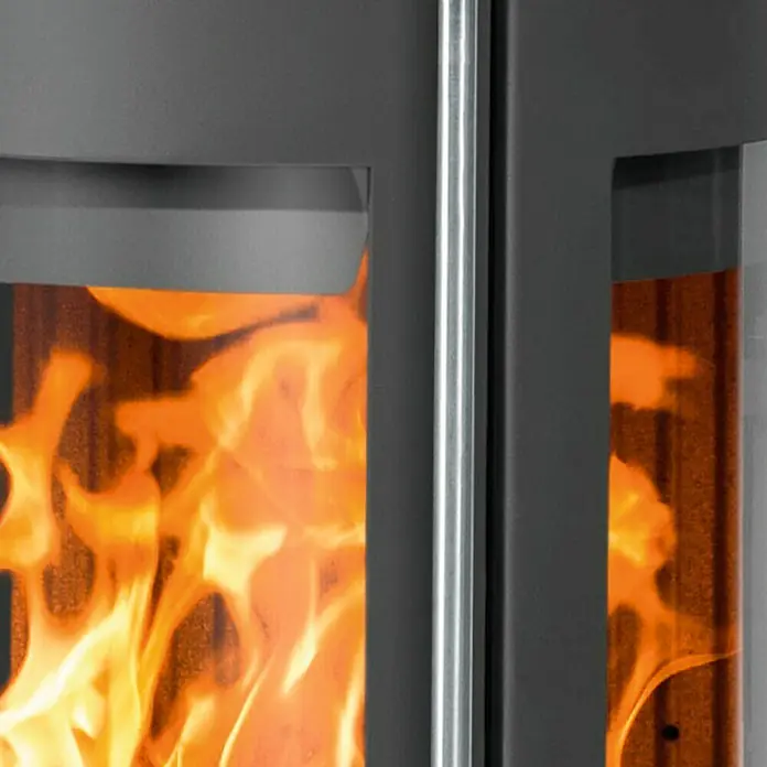 Justus Kaminofen Mino Trios 2.0 - 5,5 kW, Raumheizvermögen: 88 m³, Farbe Verkleidung: Schwarz, Schwarz - Nahaufnahme eines Kaminofens mit brennendem Feuer hinter einer Glasscheibe.