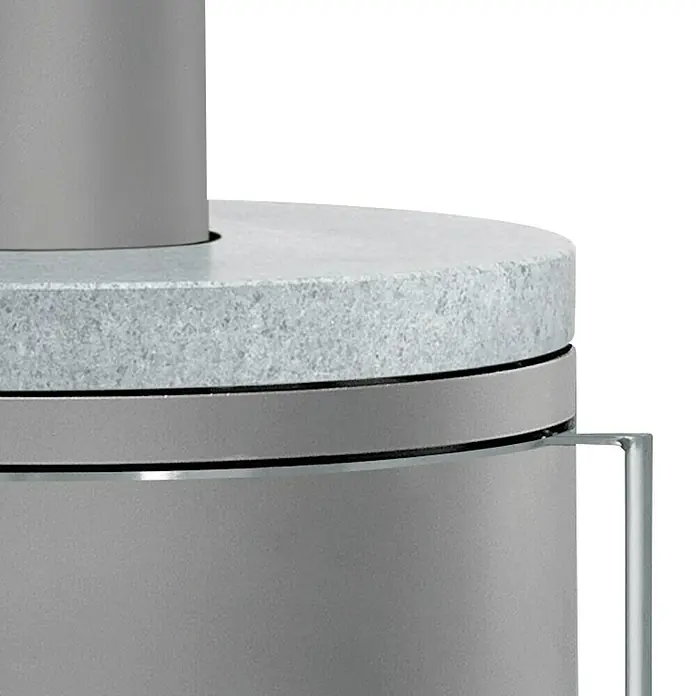 Justus Kaminofen Faro 2.0 - 6 kW, Raumheizvermögen: 115 m³, Verkleidung: Gusseisen/Speckstein, Speckstein - Nahaufnahme eines grauen Kaminofens mit runder Steinplatte und Metallakzenten, der ein modernes und stilvolles Design zeigt.