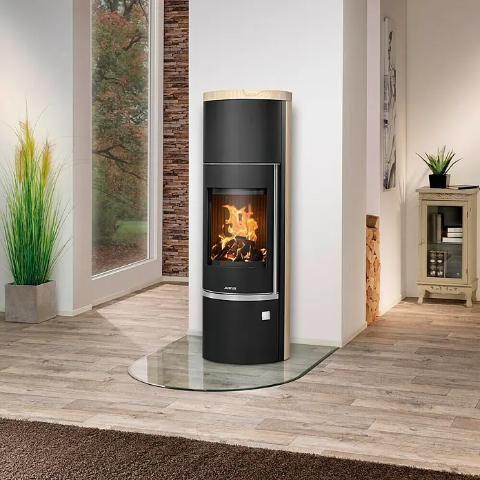Justus Kaminofen Faro W+ 2.0 - 7 kW, Raumheizvermögen: 144 m³, Verkleidung: Sandstein, Schwarz - Elegantes Wohnambiente mit einem schwarzen Justus Kaminofen, der Wärme und Stil in den Raum bringt. Die Glasplatte schützt den Boden und unterstreicht das moderne Design.
