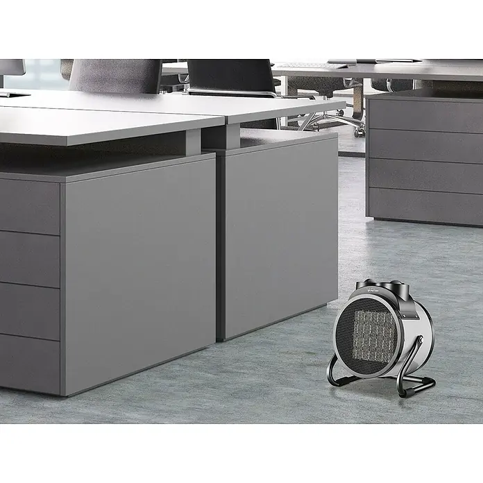 Purline Calefactor industrial HOTI F3000 - 1.500 kW - 3.000 kW - Una toma cercana de un calefactor eléctrico en un entorno de oficina. El calefactor es redondo y presenta un diseño moderno con marco metálico.