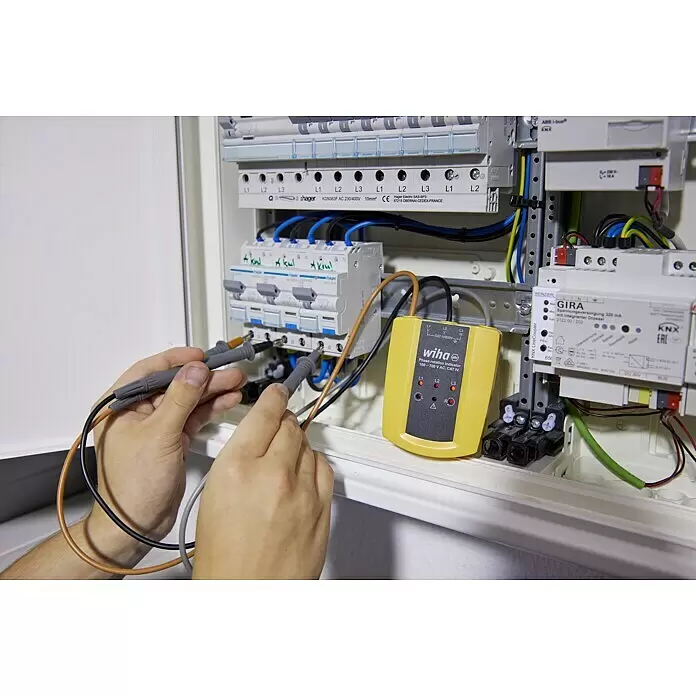 Wiha Probador de fase y campo giratorio 45221 - Categoría de medición: CAT IV 600 V - Una persona prueba un cuadro eléctrico con un indicador de rotación de fase Wiha amarillo y negro.