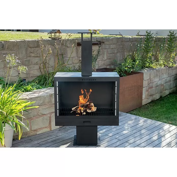 Westmann Grillkamin - L x B x H: 500 x 300 x 1.600 mm, Stahl, Schwarz - Schwarzer Metall-Außenkamin mit brennendem Holz, auf einer Holzterrasse im Garten.