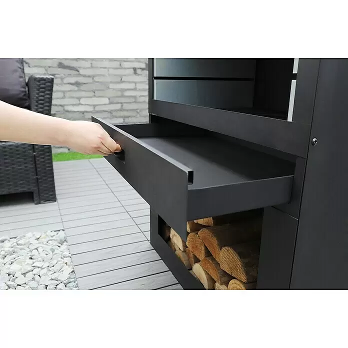 Westmann Grillkamin - L x B x H: 410 x 700 x 2.290 mm, Schwarz, Stahl - Eine Hand öffnet die Schublade einer schwarzen Outdoor-Feuerstelle mit Holzfach.