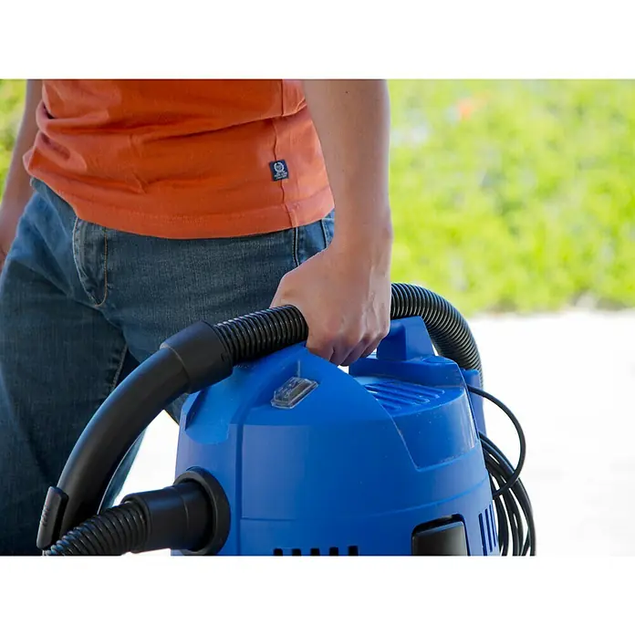 Nilfisk Aspirador en seco y húmedo eléctrico Buddy II 18 - 1.200 W, Volumen de recipiente: 18 l, Con bolsa - Una persona sostiene una aspiradora azul para sólidos y líquidos con manguera negra.