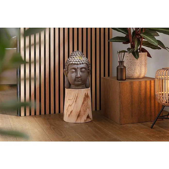 Buddhakopf Magnesia - 20 x 28 cm, Braun - Nahaufnahme einer Buddha-Kopf-Skulptur auf einem Holzsockel, daneben eine Zimmerpflanze und eine dekorative Lampe in einem stilvollen Interieur.