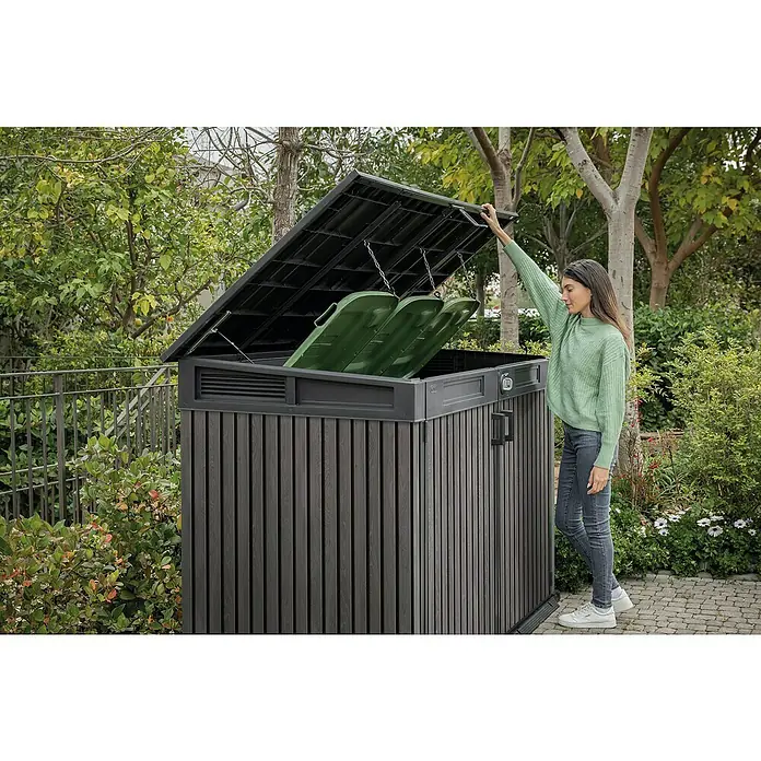 Keter Truhe Signature Venetian Grande Store - L x B x H: 109,3 x 190,5 x 132 cm, Grau - Eine Frau öffnet eine graue Mülltonnenbox mit zwei grünen Mülltonnen darin, umgeben von üppigem Grün.