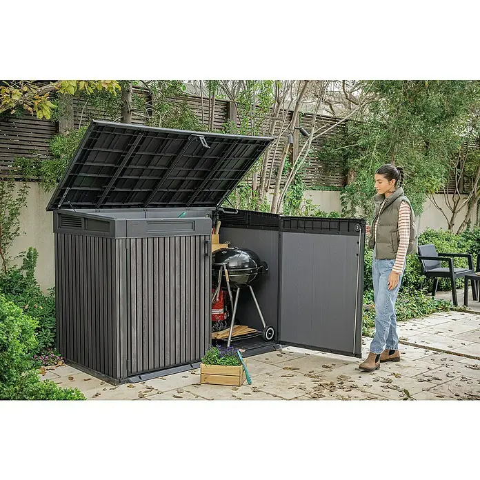 Keter Truhe Signature Venetian Grande StoreL x B x H: 109,3 x 190,5 x 132 cm, Grau - Eine stilvolle, dunkle Outdoor-Aufbewahrungsbox mit geöffnetem Deckel und einer Frau davor, ideal für Gartenutensilien und Grillzubehör.