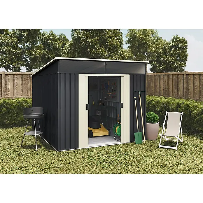 Hoggar Gerätehaus Karlstadt - Außenmaß inkl. Dachüberstand (B x T): 238 x 322 cm, Anthrazit, Stahl, Grundfläche: 7,6 m² - Ein geräumiger Gartenschuppen aus Metall mit offenem Eingang, flankiert von Grill, Schaufel und einem Klappstuhl auf einem Rasen.