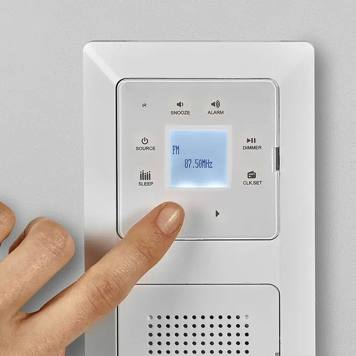 Voltomat Unterputz-Radio Bluetooth - Weiß, Glänzend, Kunststoff, 10 A - Nahaufnahme eines weißen Wandradios mit einer Hand, die den Touchscreen bedient und FM 87.50MHz anzeigt.