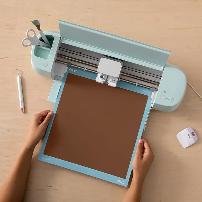 Cricut Vinylfolie Musterset Permanent - 10 Stk., Hautfarben, 30,5 x 30,5 cm - Nahaufnahme eines Cricut Schneideplotters mit Zubehör und einer Matte mit braunem Bastelpapier.