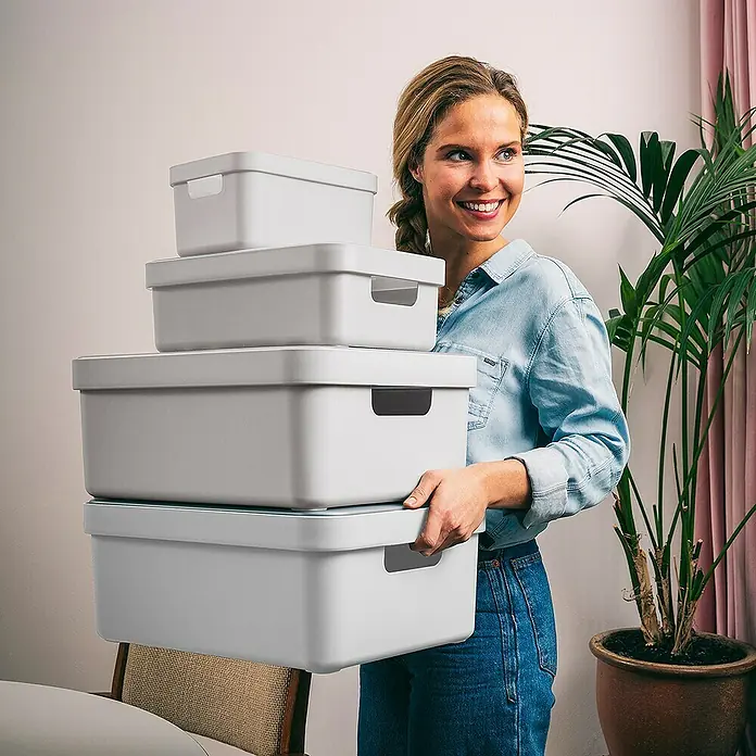 Sunware Aufbewahrungsbox Sigma Home - L x B x H: 35 x 24,6 x 12,2 cm, Kunststoff, Weiß - Frau trägt einen Stapel grauer Aufbewahrungsboxen mit Deckel verschiedener Größen. Ideal zum Ordnen und Aufbewahren von Gegenständen im Haushalt.