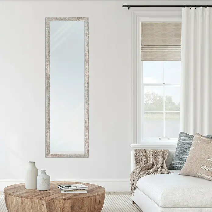 Espejo de pared Lincoln - 45 x 147 cm, Gris - Un espejo de pared alto y delgado con un marco de madera desgastada cuelga en una pared blanca, reflejando la luz del día en la habitación.