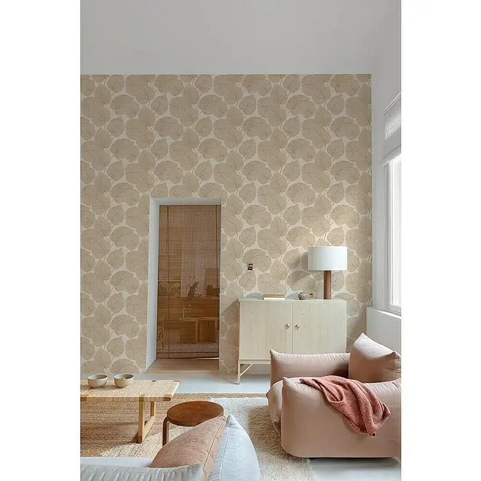 Papel pintado Hojas Vegetal - Marrón, 10 x 0,53 m - Acogedora sala de estar con papel pintado beige con motivos de hojas, armario de madera clara y un cómodo sillón rosa que crea un ambiente acogedor.