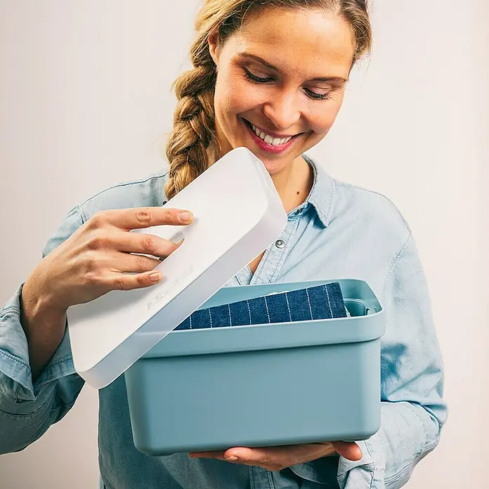 Sunware Deckel Sigma Home - Passend für: Sigma Home Aufbewahrungsbox 5 l, Kunststoff, Transparent - Eine lächelnde Frau öffnet eine hellblaue Aufbewahrungsbox mit einem weißen Deckel, in der sich gefaltete Kleidung befindet.