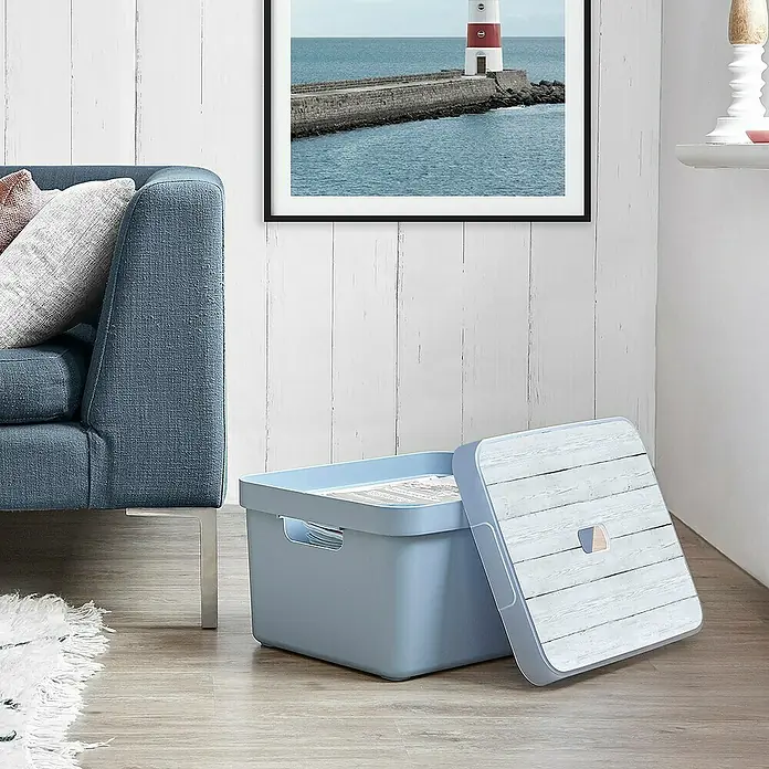 Sunware Aufbewahrungsbox Sigma Home - L x B x H: 44,5 x 34,5 x 24,3 cm, Kunststoff, Blaugrau - Blauer Aufbewahrungsbehälter mit Holzdeckel auf dem Boden neben einem Sofa. Ideal für die Organisation von Wohnräumen und die Aufbewahrung von Gegenständen.