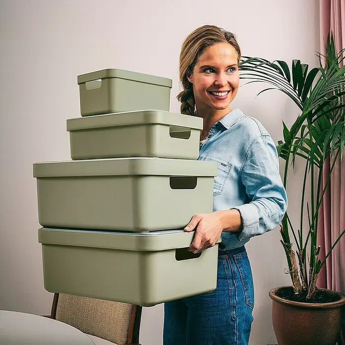 Sunware Aufbewahrungsbox Sigma Home - L x B x H: 44,5 x 34,5 x 18,3 cm, Kunststoff, Hellgrün - Frau trägt einen Stapel olivefarbener Aufbewahrungsboxen. Diese praktischen Behälter sind ideal zur Aufbewahrung verschiedener Gegenstände.