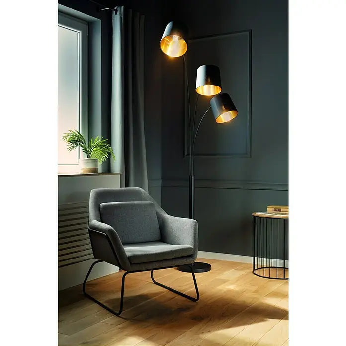 Tween Light Stehleuchte Cremona - 120 W, Höhe: 210 cm, Mattschwarz, Mattschwarz, Gold, E14 - Eine moderne Stehlampe mit drei Lampenschirmen in Schwarz und Gold, neben einem grauen Sessel und einem Beistelltisch.
