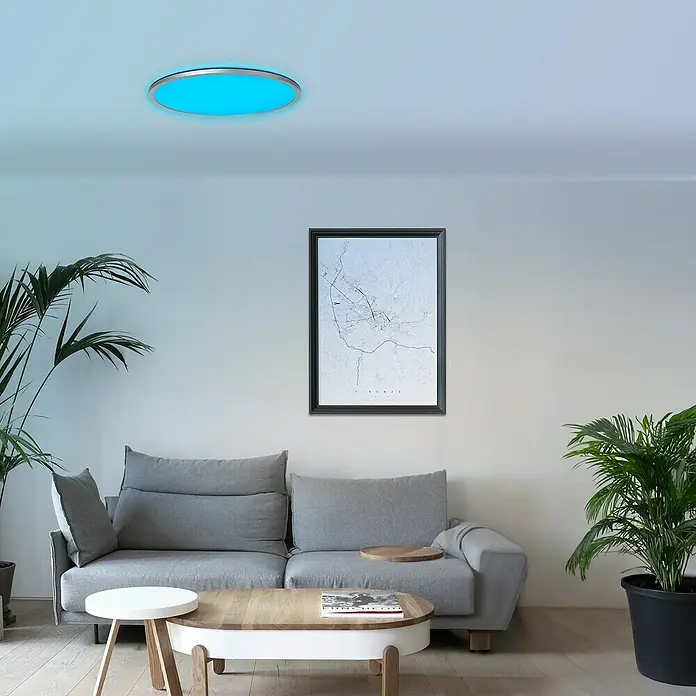 Brilliant LED-Deckenleuchte rund Tanida - 46 W, Ø x H: 57 x 3,2 cm, Silber, RGBW - Moderne Wohnzimmeransicht mit einem grauen Sofa, einem Couchtisch und einer blauen LED-Deckenleuchte, die für ein angenehmes Ambiente sorgt.